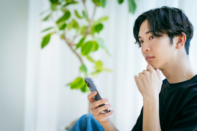スマホを手に考える男性