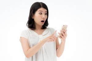 スマホを見ながら驚く女性
